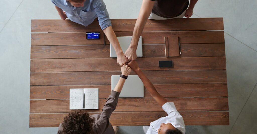 A diverse group of professionals engaging in a teamwork celebration with a fist bump over a wooden table indoors.