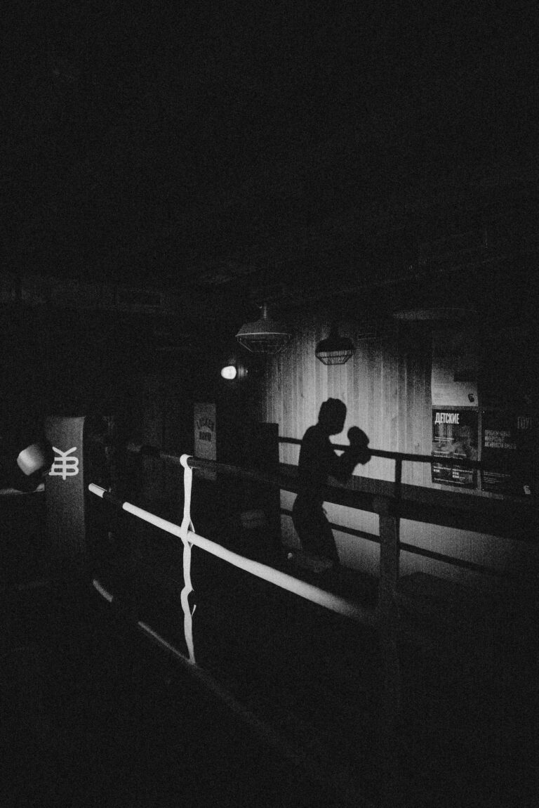 A striking monochrome silhouette of a boxer shadowboxing in a dimly-lit gym